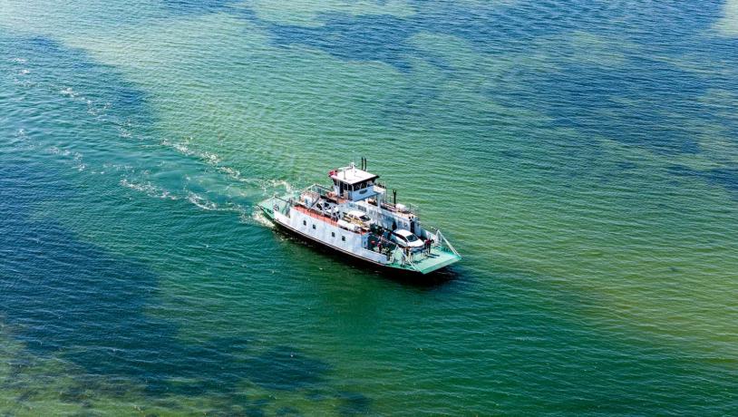 Columbus færgen sejler på åbent, grønt hav med biler og passagerer ombord set fra oven.