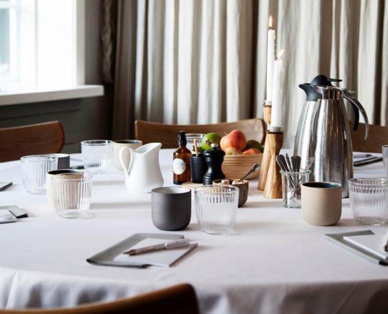 Opdækket mødebord i Herthadalen med kaffekande, glas, keramikkrus, frugtskål og blokke til notater.