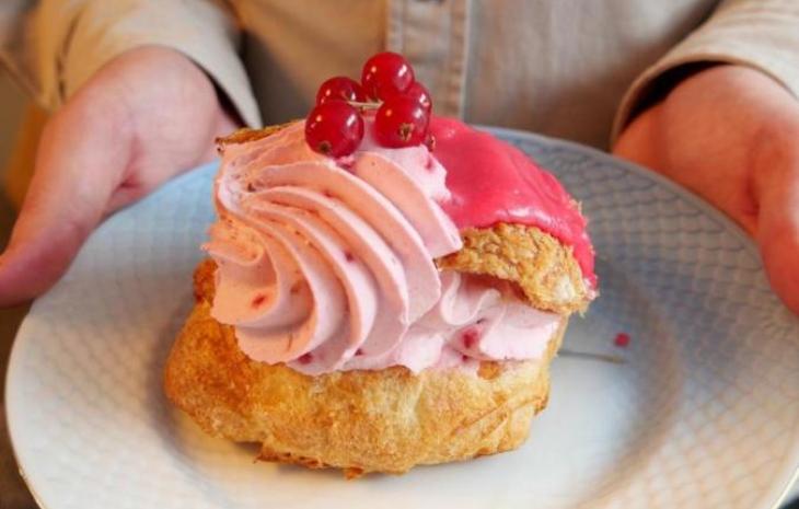 En person holder en tallerken med en fastelavnsbolle med lyserød creme og ribs på toppen.