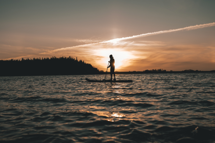 En mands silluet  stående på paddleboard i Roskilde Fjord med en solnedgang bag sig.